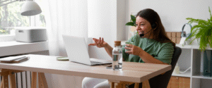 mulher com xícara na mão e fone de ouvido na frente do computador indicando bem-estar no trabalho híbrido