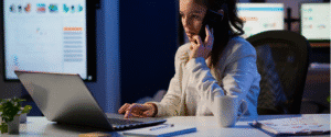 mulher com um telefone no ouvido e mexendo em um notebook conferindo o gerenciamento de dispositivos no trabalho híbrido