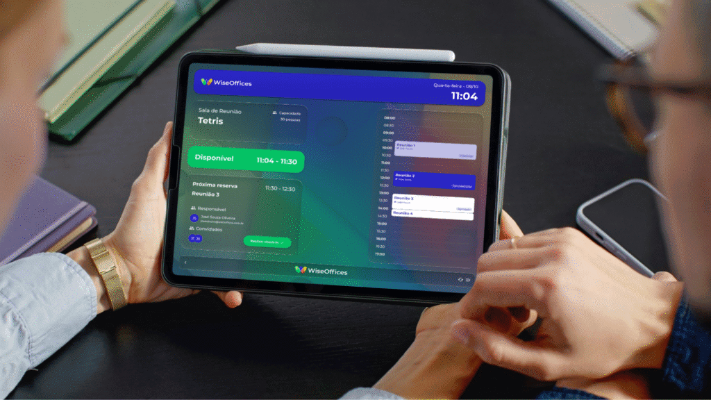Tablet exibindo interface de sinalização digital para gestão de espaços em escritório, com informações sobre disponibilidade e agendamentos.